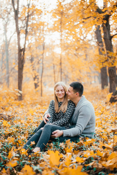 happy young couple sitting together on yellow leaves in autumn forest - Foto, Imagen