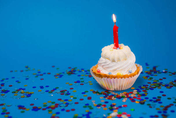 zblízka pohled na lahodný slavnostní cupcake s hořící svíčkou a barevné konfety na modrém pozadí - Fotografie, Obrázek