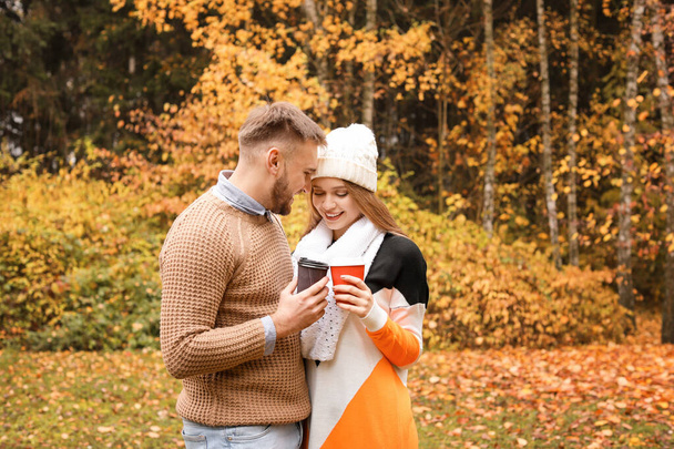 Loving young couple with cups of hot coffee in autumn park - Fotografie, Obrázek