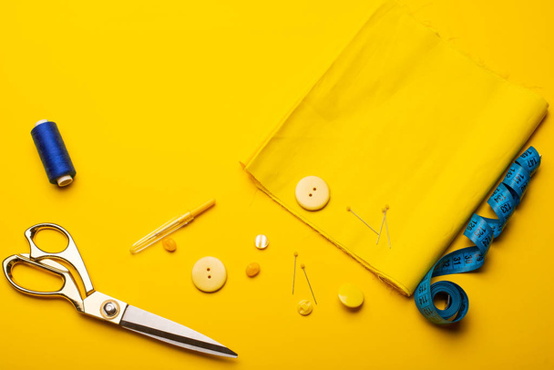 close-up view of sewing accessories, scissors, buttons, fabric and measuring tape on yellow background - Foto, imagen