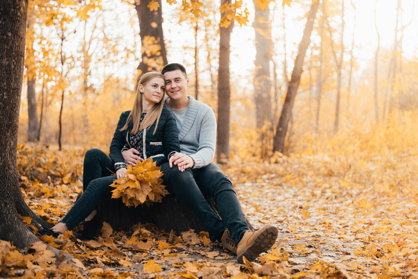 beautiful happy young couple sitting together in autumn park - Foto, afbeelding