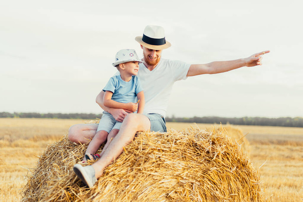 happy father with son sitting together on haystack in field - Foto, imagen