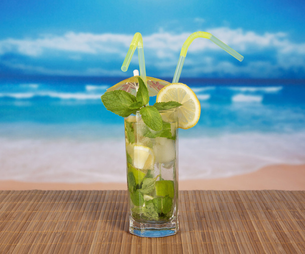 Mojito with cocktail straws and a lemon slice, on a bamboo cloth against the sea - Fotoğraf, Görsel