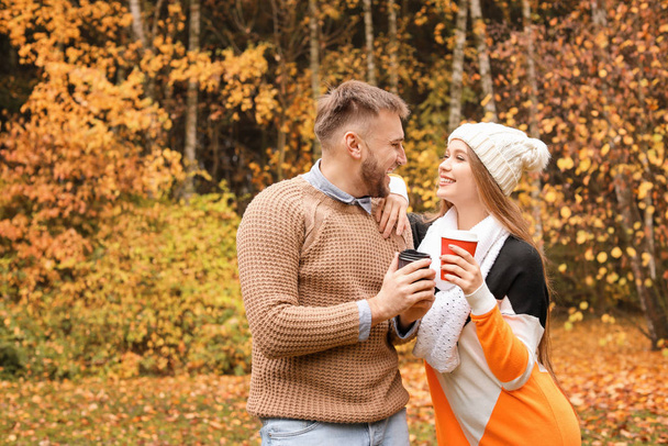 Amar pareja joven con tazas de café caliente en el parque de otoño
 - Foto, Imagen