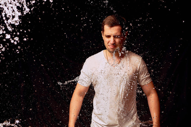 Splashes of water on the young man on dark background - Foto, Imagem