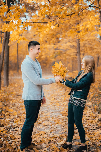 beautiful happy young couple holding orange leaves in autumn park - Fotó, kép