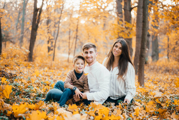 beautiful happy young family with one child sitting together in autumn park - Photo, Image