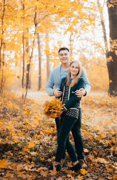 happy young couple standing together and hugging in autumn forest - Foto, afbeelding