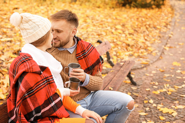 Loving young couple drinking hot tea in autumn park - Foto, Bild