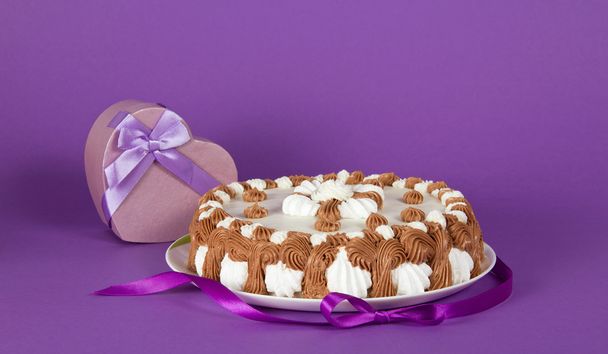 Gateau on a dish decorated with a tape and a souvenir on a violet background - Fotoğraf, Görsel