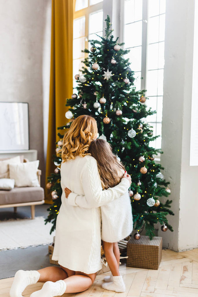 A girl with her mother near the Christmas tree, the interior decorated for the new year and Christmas, family and joy, traditions - Foto, Imagen