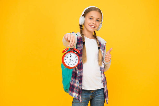 Beginning of lessons. Time go school. School time. Happy girl hold alarm clock counting minutes. Knowledge day. Classes schedule. Schoolgirl hold alarm clock yellow background. School timing concept - Фото, зображення