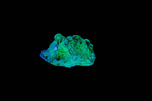 Makro-Mineralstein-Opal unter UV-Licht auf schwarzem Rücken - Foto, Bild