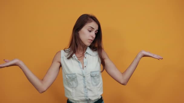 Μπερδεμένη λευκή νεαρή γυναίκα απλώνει τα χέρια της απομονωμένα στον πορτοκαλί τοίχο. - Πλάνα, βίντεο