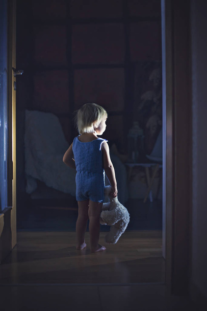 Toddler boy, hodling teddy bear, standing in hallway next to the - Foto, afbeelding