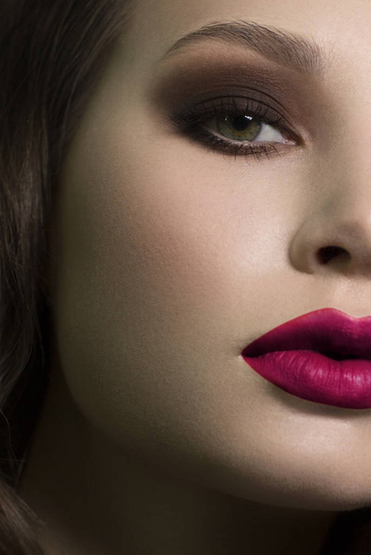 Half a beauty portrait with beautiful fashionable evening make-up, black smoky eyes and extremely long eyelashes. pink lipstick on the lips. Cosmetology and spa facial skin care - Foto, afbeelding