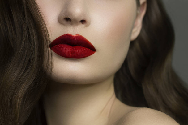 Close-up of woman's lips with fashion natural red lipstick makeup. Macro sexy pale lipgloss make-up . Gentle pure skin and wavy brunet hair. Cosmetology, Spa, increase in lips - Фото, зображення