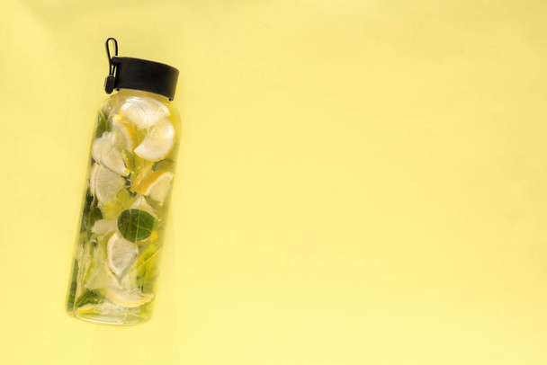 Bouteille d'eau en verre avec agrumes, citron, feuilles de menthe sur fond jaune clair. Cocktail frais, boisson de désintoxication pour remise en forme. Concept alimentation saine, alimentation. Vue du dessus, espace de copie
 - Photo, image