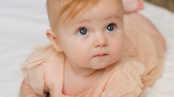Beautiful Smiling Baby: A gorgeous little baby girl lies on white blanket and smiles at the camera with a nice big eyes. close up 4k video - Filmagem, Vídeo