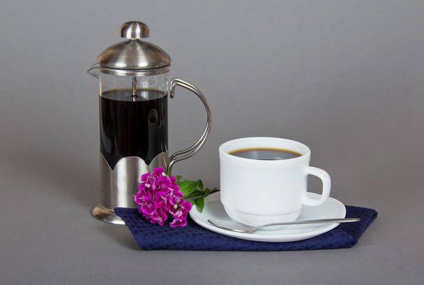 Coffee maker, cup of coffee, bright carnation, spoon and napkin on a gray background - Photo, image