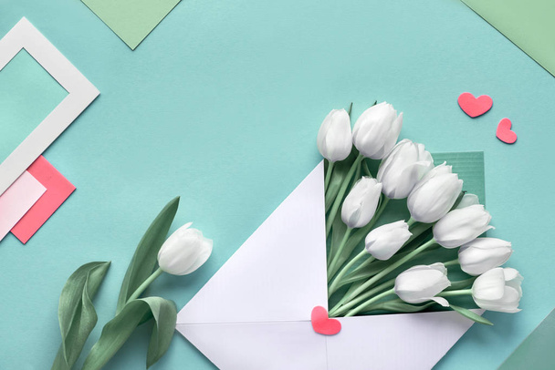 White tulips in paper envelope on blue mint background with envelopes, cards and decorative hearts. Geometris springtime background with copy-space. - Fotó, kép