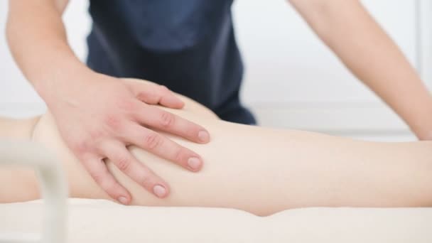 Close-up van een mannelijke fysiotherapeut doet een lichte massage om de heupen en billen van een jonge vrouw op te warmen in een professionele wellnesssalon naast een takje katoen. 4k massage lichaamsverzorging concept - Video