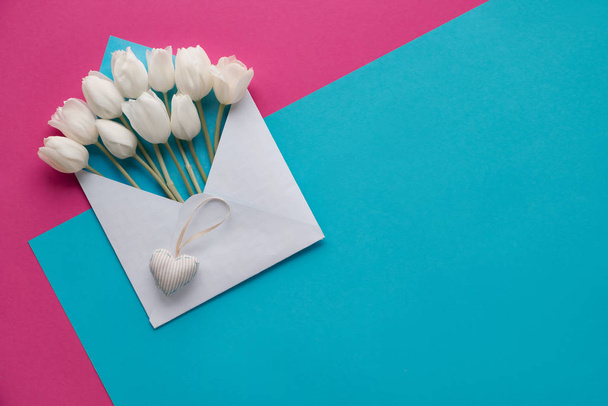Springtime flat lay, white tulips in white envelope on pink and blue  paper background, copy-space - Fotó, kép