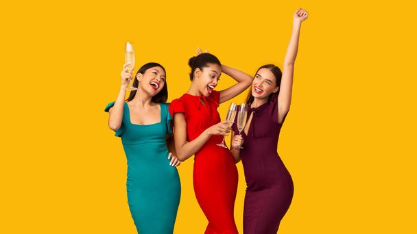 Três meninas comemorando beber vinho espumante e dançar, fundo amarelo
 - Foto, Imagem