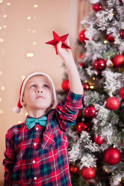 Boy's hand holding a Christmas decor big red star in a hands on the Christmas tree background - Photo, Image