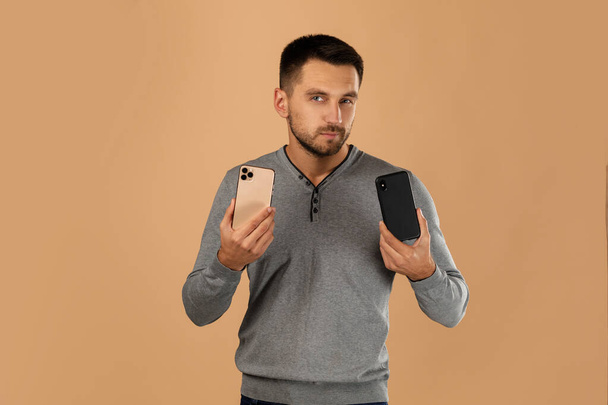 handsome young man compares two phones - Foto, imagen