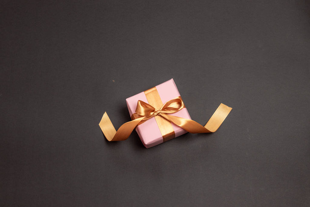 Kaunis yllätys lahja kääritty vaaleanpunainen paperi kultainen nauha rusetti tummalla pohjalla
. - Valokuva, kuva