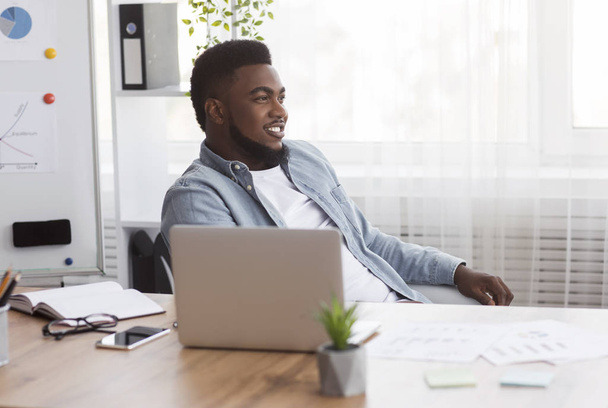 Uomo d'affari nero di successo seduto sul posto di lavoro con espressione faccia felice
 - Foto, immagini