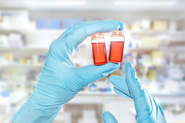 Two hands in nitril gloves hold red liquid samples in disposable plastic vials, laboratory interior out of focus - Foto, immagini
