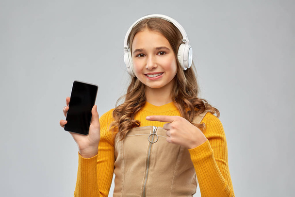 teenage girl in headphones showing smartphone - Foto, afbeelding