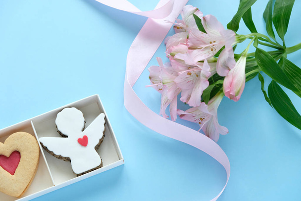 Cookies in the shape of an angel, a heart, a bear with a pink ribbon with lisianthuses on a blue background. - 写真・画像