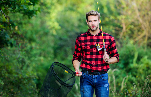 Fishing day. Handsome guy in checkered shirt with fishing equipment nature background. Fishing in my hobby. Hipster fisherman with rod spinning net. Hope for nice fishing. Summer weekend concept - Photo, image