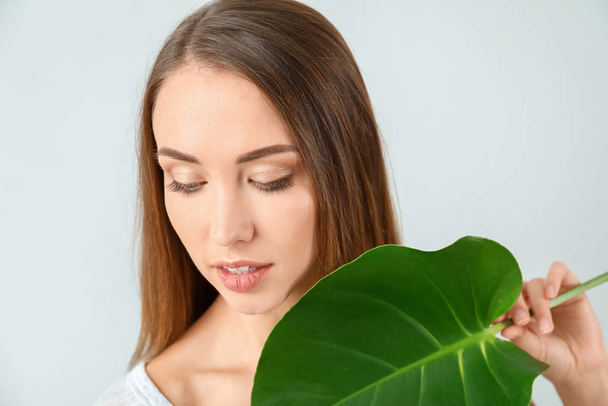 Красивая молодая женщина с тропическим листом на светлом фоне
 - Фото, изображение