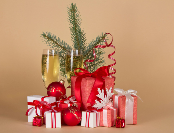 Gift boxes, toys, Christmas tree, serpentine, snowflake and wine glasses with champagne on a beige background - Photo, image