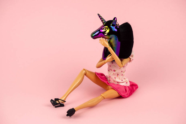 plastic woman doll in pink dress sitting with unicorn head holographic sculpture on her head isolated on a soft pink background - Foto, imagen