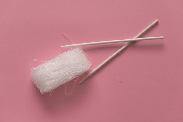 Asian uncooked cellophane noodles  with wooden chopsticks on a pink background top view flat lay - Fotó, kép