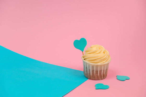 cute cupcake with butter cream decorated with a blue heart on a blue and pink background copy space - Fotoğraf, Görsel