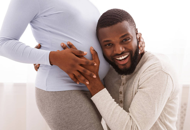 Happy husband listening to his pregnant wife belly at home - Фото, изображение
