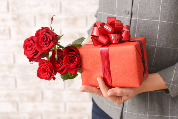 Woman with gift for Valentine's Day and flowers on brick background, closeup - Фото, зображення