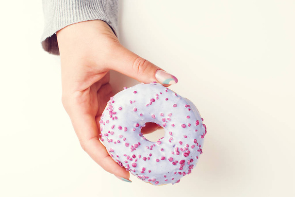 Hand met lekkere donut, bovenaanzicht. Kleurrijke zoete donut met hagelslag. Manicure. Hand met gekleurde pastelnagels - Foto, afbeelding