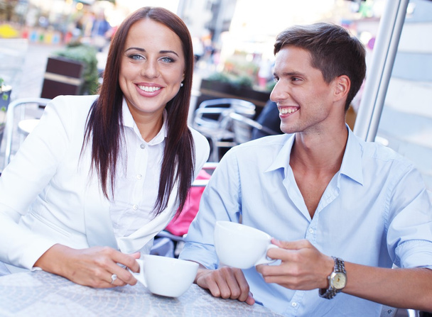 Молодая пара с чашками сидя в летнем кафе
 - Фото, изображение