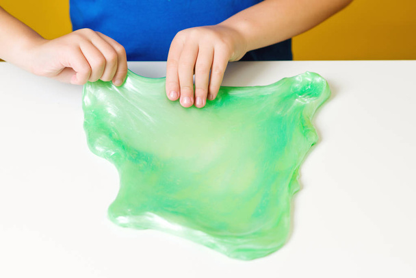 Lapsi leikkii vihreällä limalla valkoisella pöydällä, ylhäältä. Moottorioppilaiden taidot. Luovuus ja kehitys
 - Valokuva, kuva