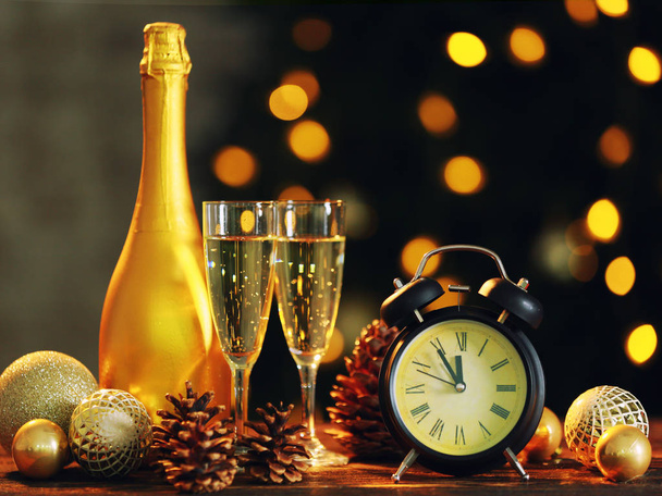 Alarm clock with Christmas decor and champagne on table against defocused lights - 写真・画像