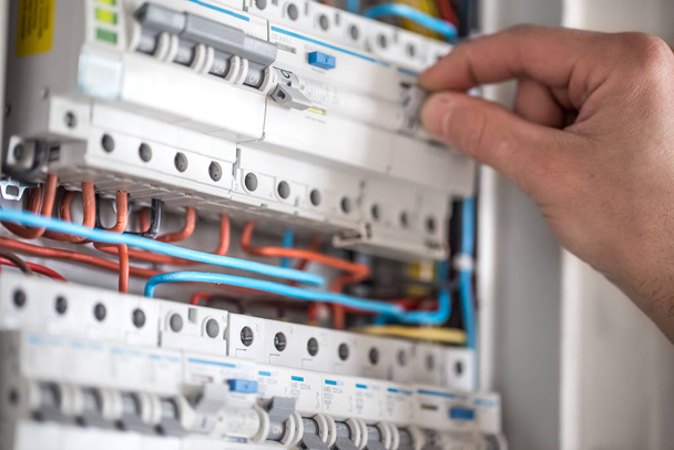 Man, an electrical technician working in a switchboard with fuses. Installation and connection of electrical equipment. Close up. - 写真・画像