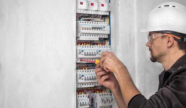 Hombre, un técnico eléctrico trabajando en una centralita con fusibles. Instalación y conexión de material eléctrico
. - Foto, imagen