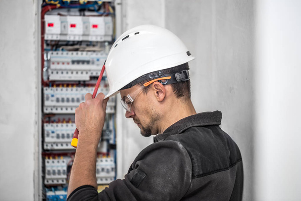 Mann, ein Elektrotechniker, der in einer Schaltanlage mit Sicherungen arbeitet. Installation und Anschluss von elektrischen Geräten. - Foto, Bild